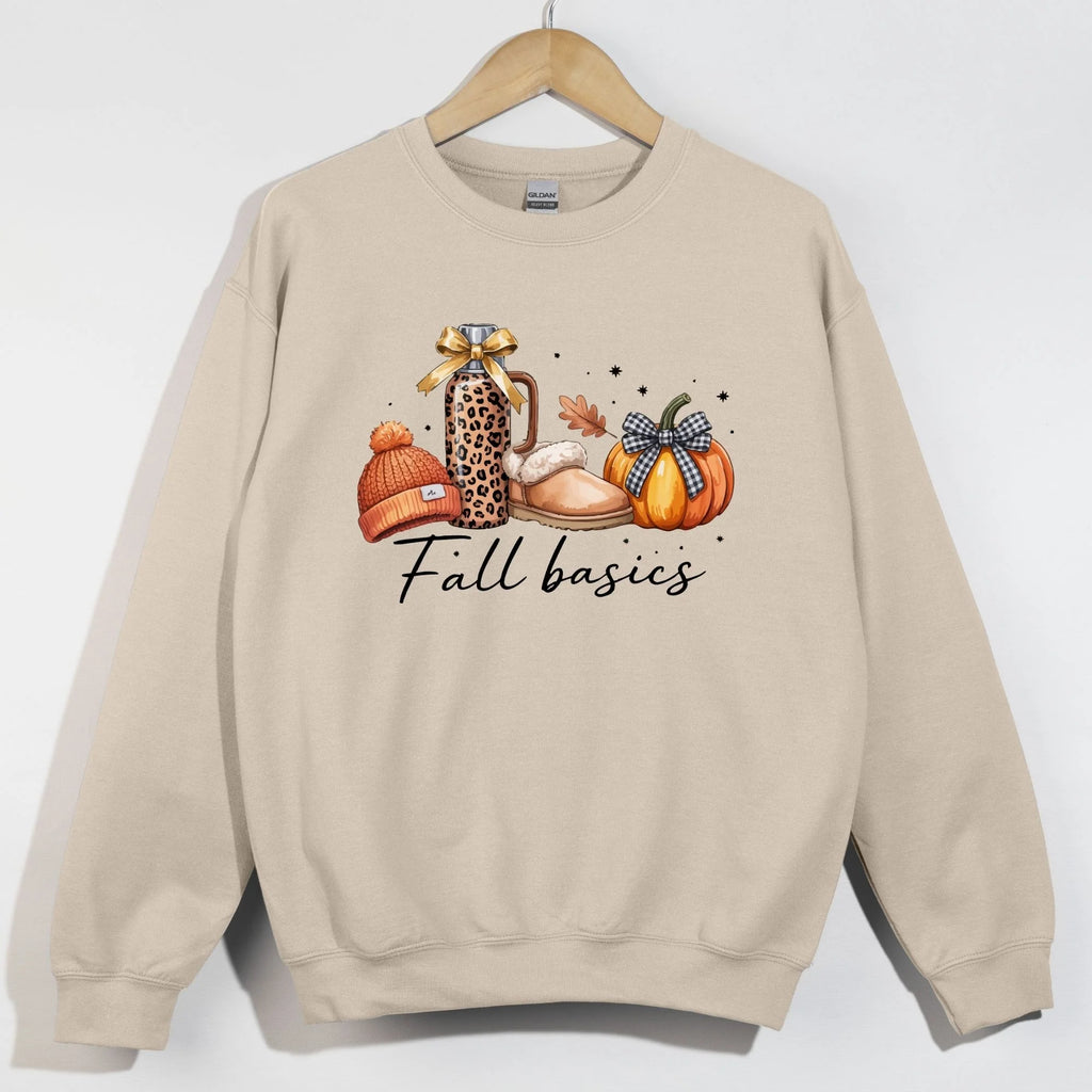 Sand Gildan crewneck sweatshirt with Fall basics graphic featuring leopard Stanley tumbler, UGG slippers, orange pom beanie, and buffalo plaid pumpkin