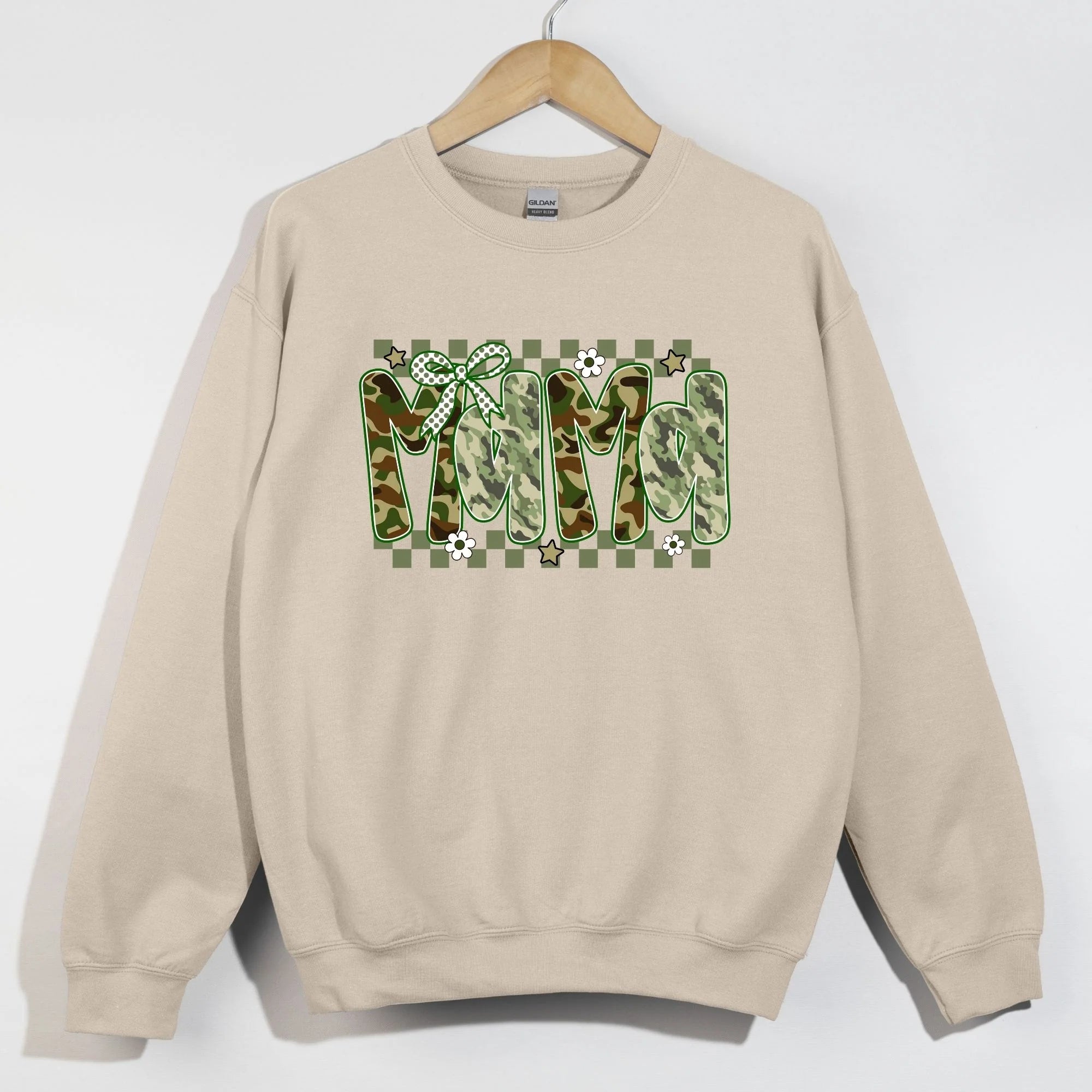 Sand Gildan crewneck sweatshirt on hanger with MAMA in camo patterned bubble letters on green checkered background with polka dot bow daisies and stars