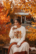 Woman wearing ivory Comfort Colors mama fall leaves bow patterned letters long sleeve tee outdoors in autumn setting with warm golden light