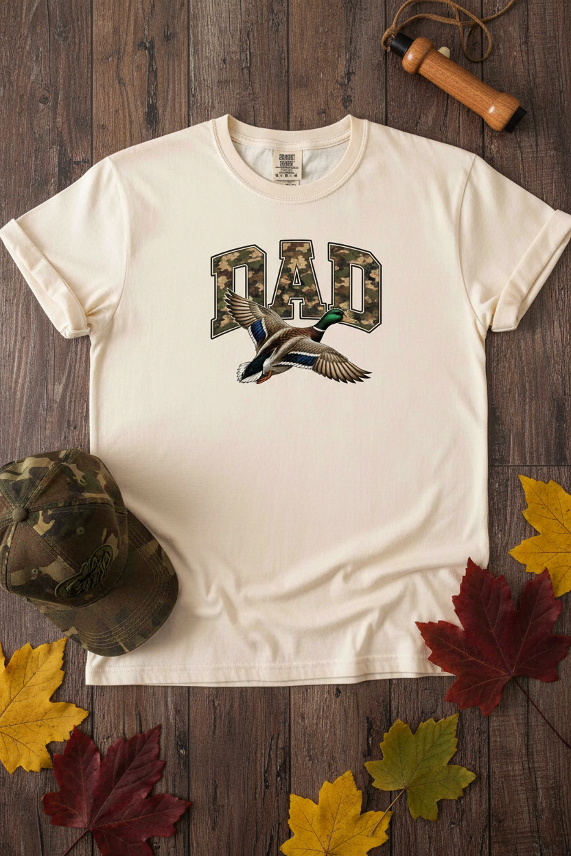 Camo Duck Dad T-Shirt styled with duck call, camo cap, and autumn leaves on rustic wood